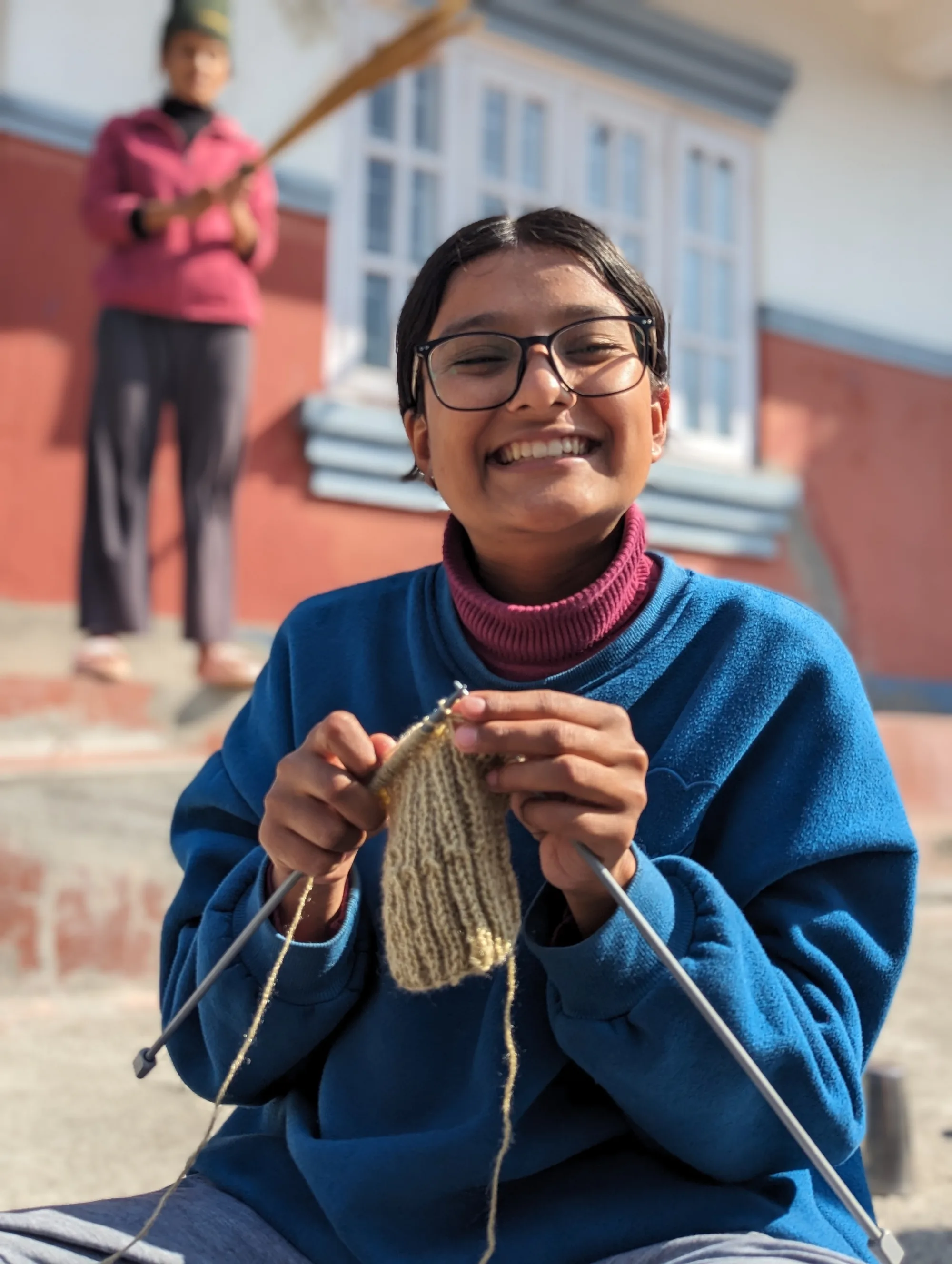 A female scholar at Pestalozzi International India knitting and smiling