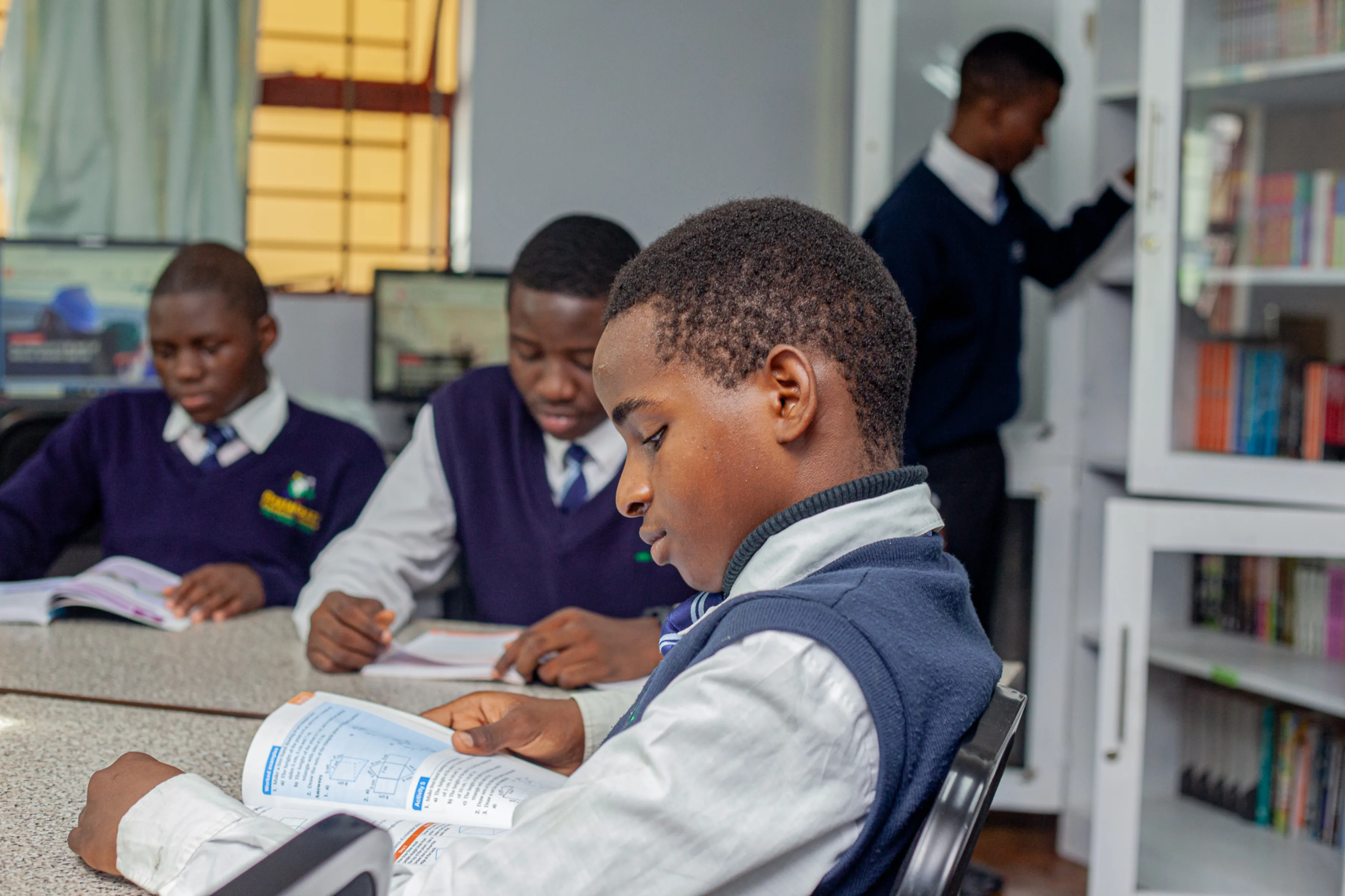 Three young male students sitting on a table in the library of Pestalozzi International Zambia