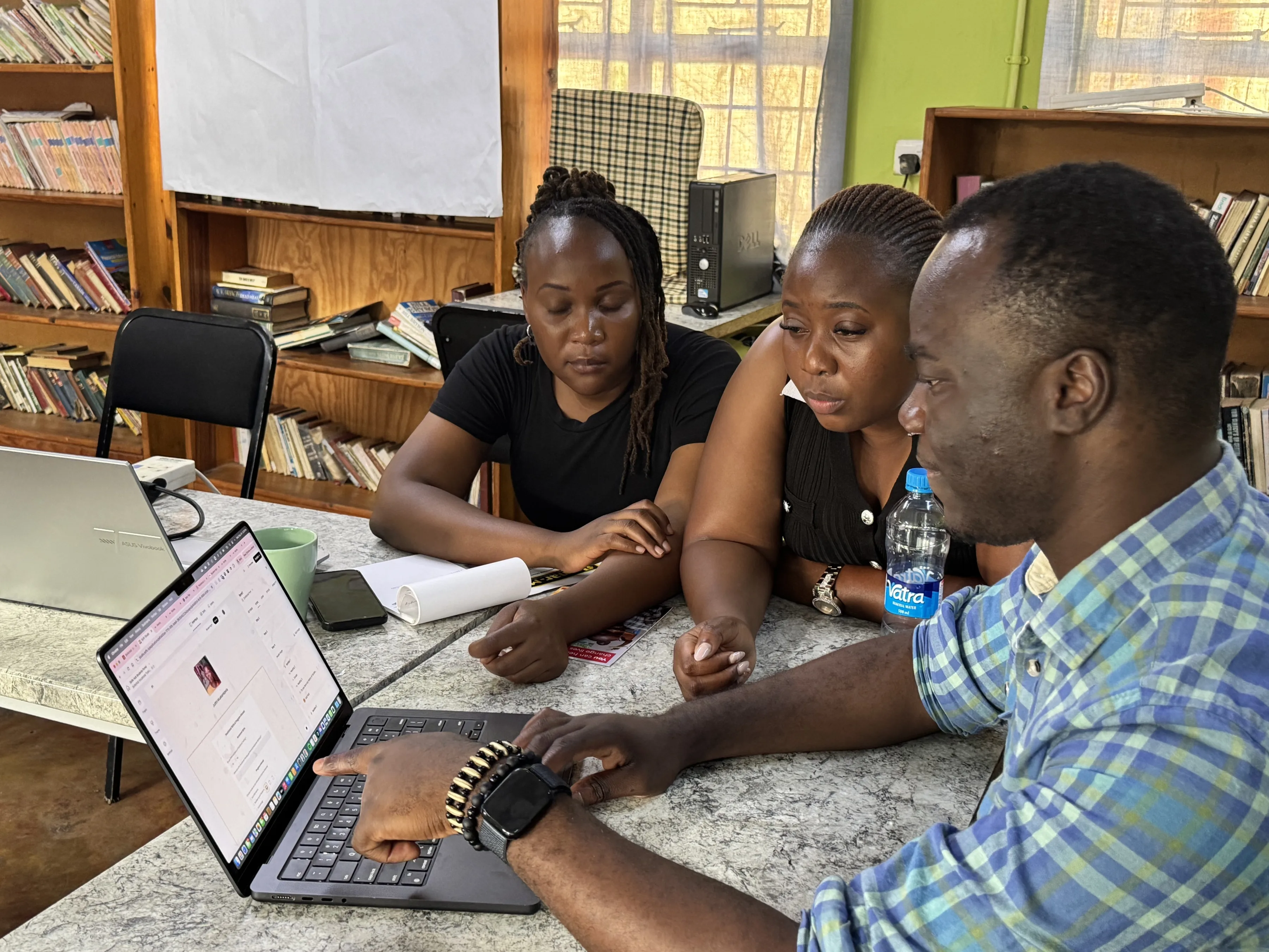 Group of staff from our team in Zambia gathered around a laptop learning about the digital world