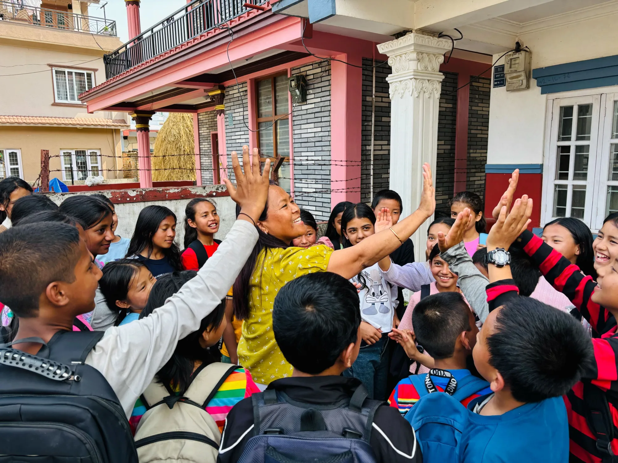 Image of Cheme, Director of India standing in a circle of a group of a least 20 students from our Nepal campus waiting to high-5 each of them. Cheme has her had up ready to high-5 individuals and students have their hands up in the air ready to receive their high-5.